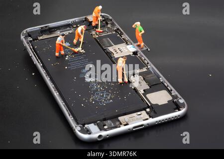Miniature workers staged inside a smartphone interior for editorial illustration. Stock Photo