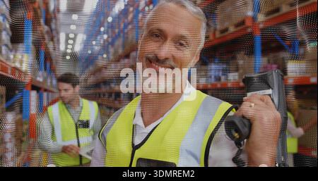 Smiling worker wearing hi-vis vest using handheld scanner in warehouse aisle with racking Stock Photo