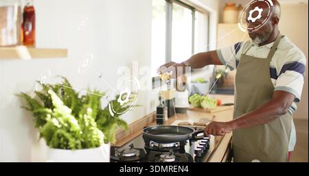 Pouring oil, senior man wearing apron cooking in home kitchen frying pan with smart UI overlay Stock Photo