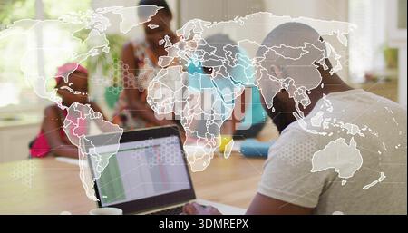 Working adult man in grey tee viewing spreadsheet on laptop at dining table, with map overlay Stock Photo