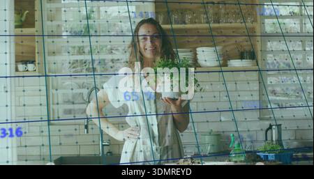 Holding potted herb plant, woman standing in kitchen wearing button shirt, with blue grid overlay Stock Photo