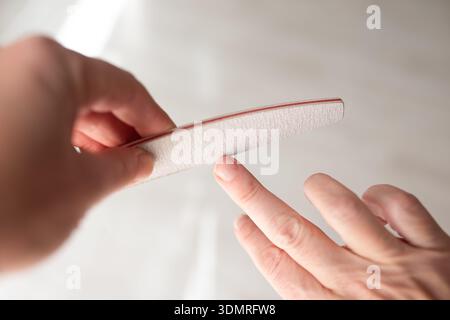 Person filing nails with professional emery board in bright room, beauty salon, self care, spa industry. Stock Photo