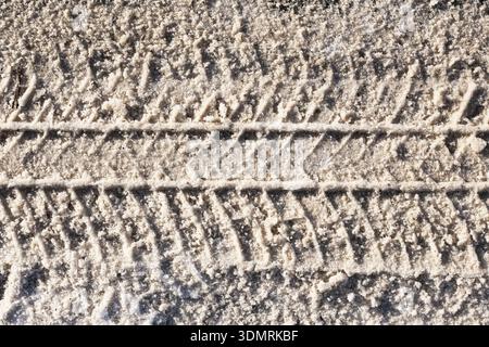 Tire tracks texture in snow closeup. Winter road surface pattern with vehicle marks and frozen outdoor background during cold season. Stock Photo