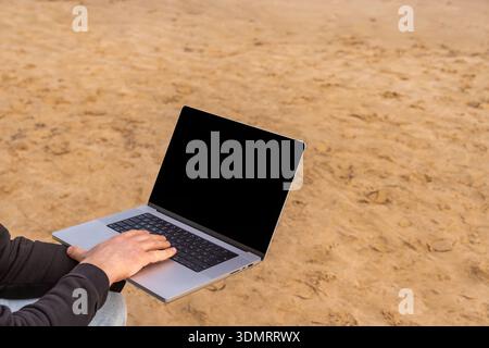 Concentrated typing at tranquil seaside under sunlight. Engaged in research and drafting on laptop near peaceful sandy coast area Stock Photo