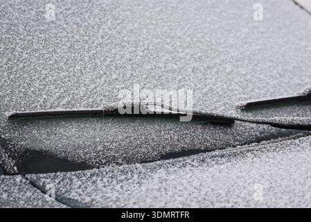 Close-up of a car windshield covered with frost and light snow, featuring frozen windshield wipers. The image represents cold winter weather, morning Stock Photo