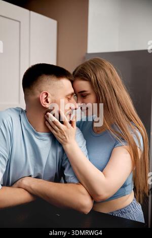 Two people lean close, sharing a moment in their kitchen at home. They smile gently at each other, enjoying an intimate connection during afternoon. Stock Photo