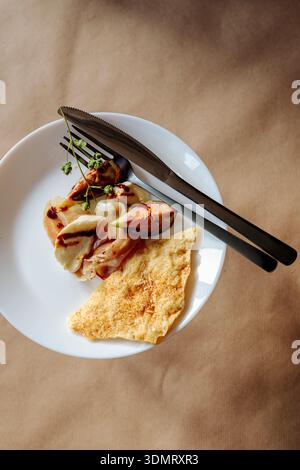 Small portion of fig and prosciutto appetizer with cracker and cutlery on white plate. Rustic craft paper background. Stock Photo