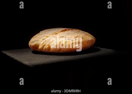 Round rustic bread loaf on black stone stand. Dark moody bakery product photography. Stock Photo