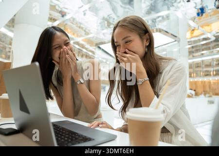Friends laughing together watching something on laptop Stock Photo