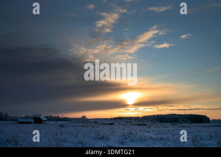 Winter Sunset over Snowy Field with Distant Cabin Stock Photo