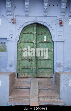 A weathered green door set against a blue wall in a traditional setting. Stock Photo