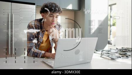 Leaning man, plaid shirt, mustard tee, working on laptop at kitchen island with HUD, copy space Stock Photo