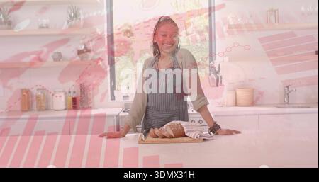 Smiling woman wearing striped apron slicing loaf on wooden cutting board in kitchen, chart overlay Stock Photo
