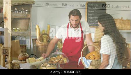 Male baker in red apron serving female client at bakery counter, wicker baskets and chalkboard Stock Photo