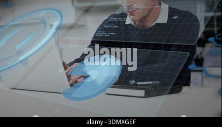 Typing mature man wearing dark sweater, at office desk using laptop with HUD overlays, notebook pen Stock Photo