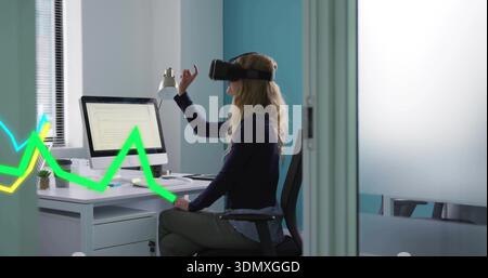 Gesturing woman wearing navy blazer and VR headset using monitor at office with neon green overlay Stock Photo