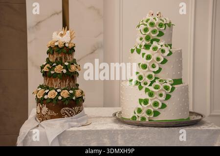 A beautifully crafted two-tier wedding cake adorned with white and green sugar flowers, swan figurines, and intricate detailing, set against marble an Stock Photo