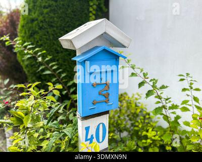 Blue bright metal mailbox hangs on white column decorated with golden keys. Stylish detail in interior of house in authentic style. Street box for let Stock Photo