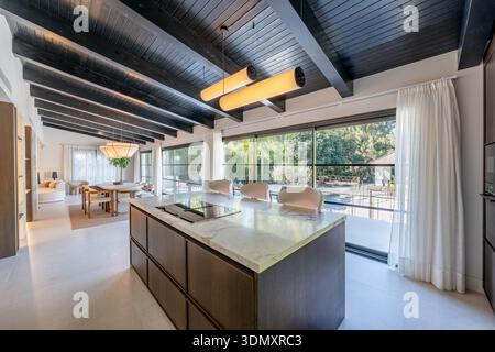 an image of a large marble kitchen island with dining area and glass windows with views of the private pool in mediterranean villa Stock Photo
