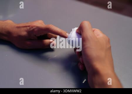 Closeup top view of male hands holding portable electric nail clipper, filing nails on gray table while performing manicure at home using modern Stock Photo