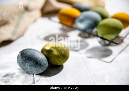 Naturally dyed easter eggs drying on a white wooden table, creating a festive atmosphere for easter celebrations, with a beige cloth in the background Stock Photo