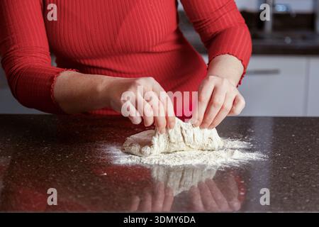 A person in a red shirt kneads pizza dough on a floured countertop. The close-up shows hands shaping the dough, highlighting the process of homemade p Stock Photo