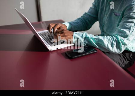 Businessman with dreadlocks working on a laptop in a modern office. The African American professional is focused, with a smartphone placed beside him Stock Photo