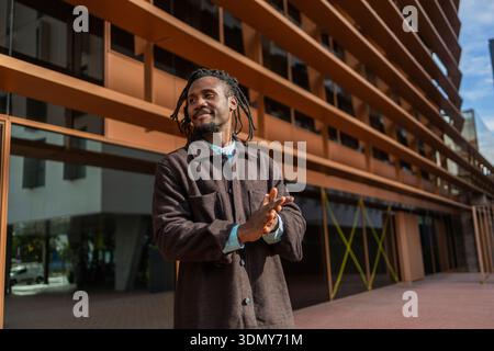 African American businessman with dreadlocks standing confidently outside a modern office building, reflecting professionalism and success in urban bu Stock Photo