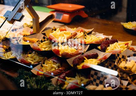 An appetizing display of street food featuring crispy fries and grilled sausages in paper trays. Accompanied by cherry tomatoes and dipping sauces, re Stock Photo