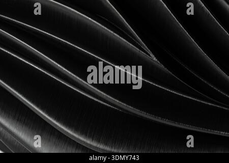Close-up of abstract black plastic waves creating a smooth, flowing background. The texture and light play over the surface, forming elegant curved li Stock Photo