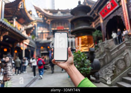 A person holds a mobile phone with a blank screen in front of intricate traditional architecture, capturing the essence of Chongqing, China's blend of Stock Photo