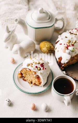 A festive Easter scene featuring a delicious cake adorned with white icing and colorful decorations. Ceramic bunnies, eggs, and tea set complete the j Stock Photo