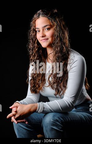 Young brunette woman with curly hair and a subtle smile against a black background Stock Photo