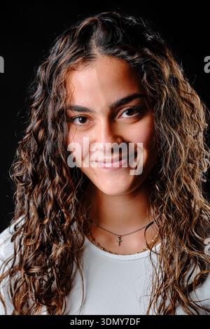 Smiling young woman with curly brown hair against a black background Stock Photo