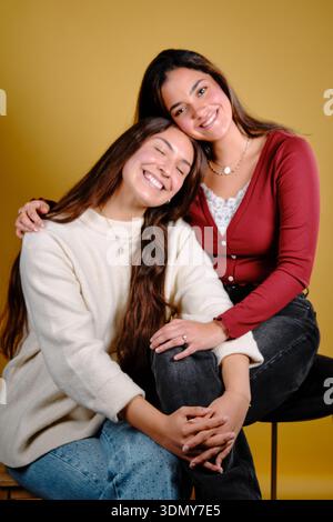 Two happy young women connecting and smiling on a yellow background Stock Photo