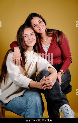 Two smiling women embracing each other against a yellow studio background Stock Photo