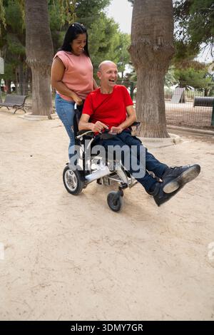 A joyful moment outdoors featuring a person in a wheelchair and their companion, highlighting inclusivity and accessibility in nature for people with Stock Photo