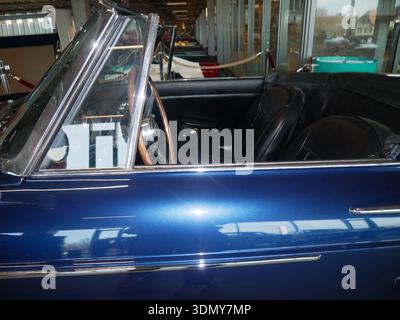Classic convertible car interior showcases black leather seats and a wooden steering wheel, set within a contemporary automotive museum environment Stock Photo