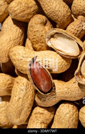 Close-up image of peanuts in their shells, highlighting the texture and natural tones. Some shells are open, revealing the whole nut inside, offering Stock Photo