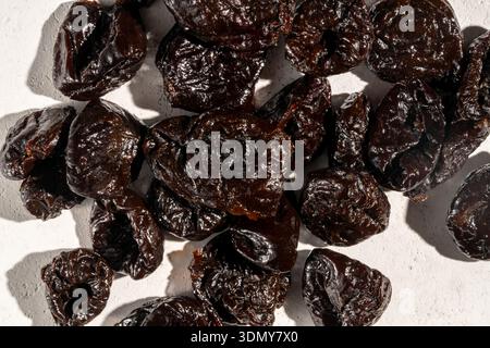 Close-up image of dried prunes on a light, textured surface. The dark, wrinkled texture of the prunes is highlighted, showcasing their rich color and Stock Photo