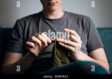 Close-up of hands skillfully crocheting with a green yarn, using a crochet hook. The concentration on the intricate needlework showcases craftsmanship Stock Photo
