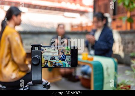A mobile phone on a tripod records a traditional tea ceremony, highlighting the cultural essence and intricate rituals. Three people are engaged in th Stock Photo