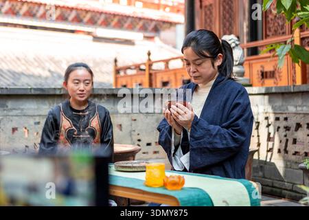 Two women perform a traditional tea ceremony outdoors, highlighting cultural heritage and ritualistic practices. One is attentively preparing tea, cre Stock Photo