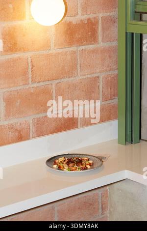 A cozy restaurant setting with warm brick walls and soft lighting, showcasing a beautifully plated dish on a countertop, creating an inviting atmosphe Stock Photo