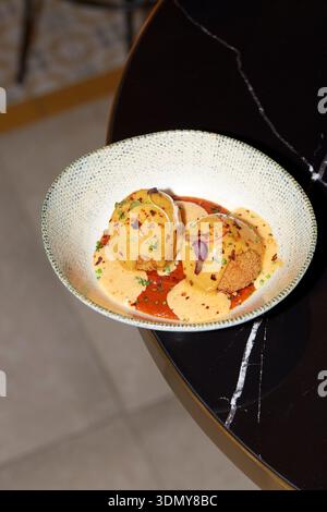 A delectable gourmet dish featuring two golden-brown spheres with a creamy sauce garnish, elegantly presented in a textured bowl on a dark, modern tab Stock Photo