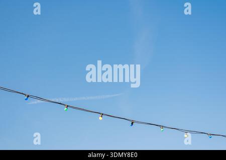A series of colorful string lights hang across a clear blue sky, casting a festive mood. The vivid bulbs contrast beautifully against the expansive, c Stock Photo