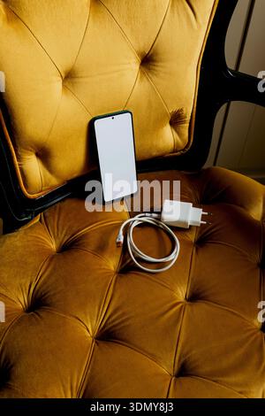 A modern smartphone and charger placed elegantly on a luxurious velvet armchair, showcasing a blend of technology and style in a cozy and sophisticate Stock Photo