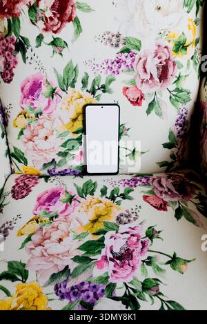 A smartphone with a blank screen rests on a vibrant floral patterned fabric. The background showcases an array of colorful flowers, creating a contras Stock Photo
