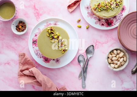 A delectable pistachio and white chocolate cheesecake served on a floral plate. The dessert is garnished with crushed pistachios, presented on a pink Stock Photo