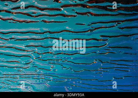 Close-up of an abstract holographic pattern on embossed glass, showcasing vibrant blue and orange hues with wavy textures creating a dynamic visual ef Stock Photo